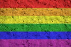 LGBT community flag depicted in bright paint colors on old relief plastering wall. Textured banner on rough background photo