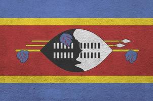 Swaziland flag depicted in bright paint colors on old relief plastering wall. Textured banner on rough background photo