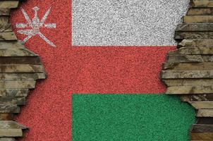 Oman flag depicted in paint colors on old stone wall closeup. Textured banner on rock wall background photo