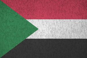 Sudan flag depicted in bright paint colors on old relief plastering wall. Textured banner on rough background photo