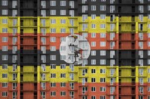 Uganda flag depicted in paint colors on multi-storey residental building under construction. Textured banner on brick wall background photo