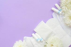 Menstrual pads and tampons with tender white flowers on pastel lilac background photo