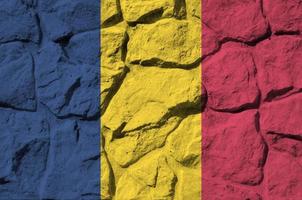 Chad flag depicted in paint colors on old stone wall closeup. Textured banner on rock wall background photo