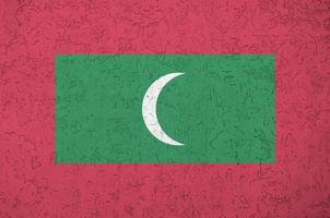 Maldives flag depicted in bright paint colors on old relief plastering wall. Textured banner on rough background photo