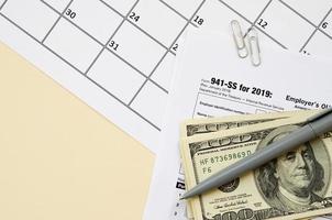 IRS Form 941-SS Employer's quarterly federal tax return blank lies with pen and many hundred dollar bills on calendar page photo