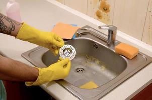 Cleaner in rubber gloves shows clean plughole protector of a kitchen sink photo