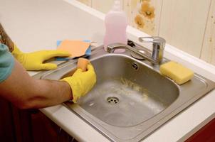 Person or householder cleaning the kitchen sink with sponge in close up view photo