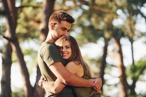 Happy together. Embracing each other. Beautiful young couple have a good time in the forest at daytime photo