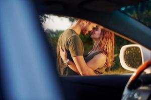 View through the car's window. Beautiful young couple have a good time in the forest at daytime photo