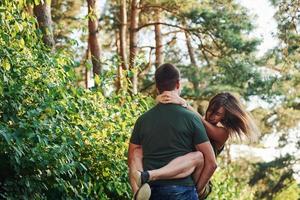 Near white colored car. Beautiful young couple have a good time in the forest at daytime photo