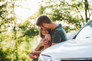 Behind the car. Beautiful young couple have a good time in the forest at daytime photo