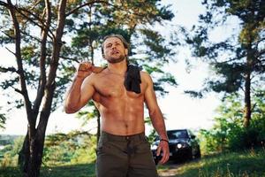 Close up portrait of woodsman with axe in hand. Handsome shirtless man with muscular body type is in the forest at daytime photo