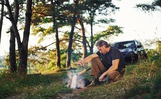 Heating by the fire. Man in black shirt near the campfire in the forest at his weekend time photo