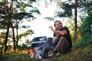 tiempo para un descanso. hombre con camisa negra cerca de la fogata en el bosque en su tiempo de fin de semana foto