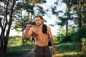 Close up portrait of woodsman with axe in hand. Handsome shirtless man with muscular body type is in the forest at daytime photo