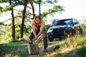 Woodsman with an axe cutting wood. Handsome shirtless man with muscular body type is in the forest at daytime photo