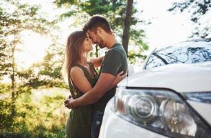 parte delantera del coche blanco. hermosa pareja joven diviértete en el bosque durante el día foto