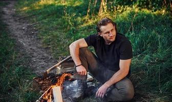 Time for a rest. Man in black shirt near the campfire in the forest at his weekend time photo
