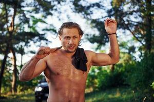 Close up portrait of woodsman with axe in hand. Handsome shirtless man with muscular body type is in the forest at daytime photo