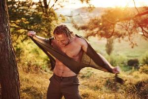 rasgando la camisa. concepción de la libertad. hermoso hombre en el bosque. buen tiempo. hermosa luz del sol de color naranja foto