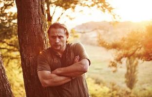 With arms crossed. Beautiful man in the forest. Good weather. Beautiful orange colored sunlight photo