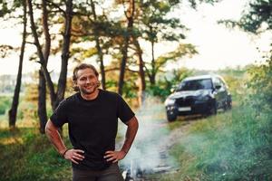 retrato de hombre que se para en el bosque y mira la naturaleza. automóvil estacionado detrás foto