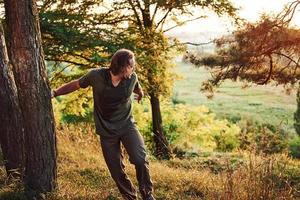 Tired traveler on the hill. Beautiful man in the forest. Good weather. Beautiful orange colored sunlight photo