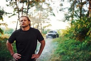 Portrait of man that stands in the forest and looks at nature. Automobile parked behind photo