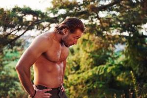 Beautiful nature. Handsome shirtless man with muscular body type is in the forest at daytime photo