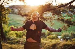 gritando y rasgando la camisa. concepción de la libertad. un hombre guapo con un tipo de cuerpo musculoso está en el bosque durante el día foto