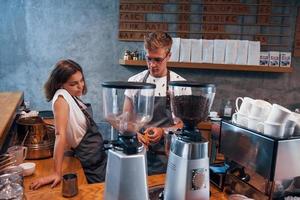 Behind the coffee machine. Two young workers indoors. Conception of business and service photo