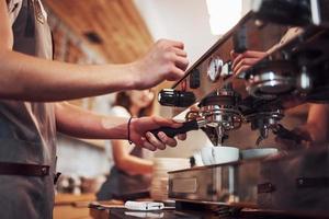 Process of making fresh drink. With machine. Two young cafe workers indoors. Conception of business and service photo