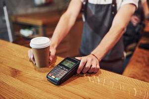 Drenaje y sistema de pago digital. joven trabajador de café masculino en el interior. concepción de negocio y servicio foto