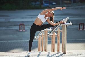 Sportive woman doing fitness exercises in the city at daytime. Near the railings photo