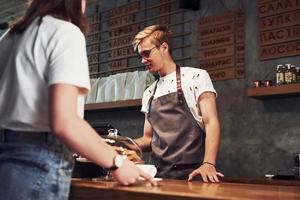 Process of paying with credit card. Young male cafe worker indoors. Conception of business and service photo