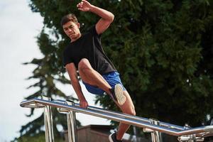 saltando por encima del obstáculo. joven deportista haciendo parkour en la ciudad durante el día soleado foto