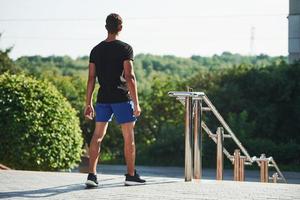 Back view of young man that stands near the railings and looks far away. New day has come photo