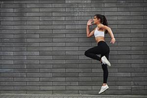 Photo in motion. Young sportive brunette with slim body shape against brick wall in the city at daytime