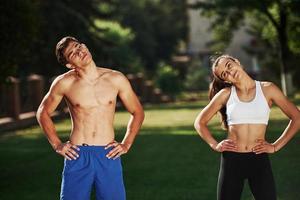Warm up exercises. Man and woman have fitness day in the city at daytime in the park photo