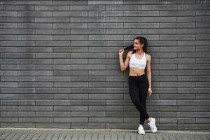 Young sportive brunette with slim body shape against brick wall in the city at daytime photo