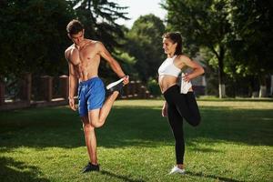 Exercises for legs. Man and woman have fitness day in the city at daytime in the park photo