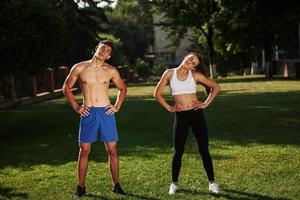 Warm up exercises. Man and woman have fitness day in the city at daytime in the park photo