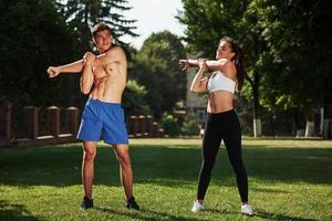 Warm up exercises. Man and woman have fitness day in the city at daytime in the park photo