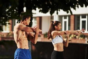 Warm up exercises. Man and woman have fitness day in the city at daytime in the park photo