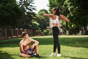 Guy sitting with smartphone in hands and have rest. Man and woman have fitness day in the city at daytime in the park photo