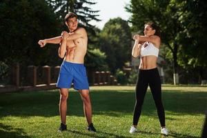 Warm up exercises. Man and woman have fitness day in the city at daytime in the park photo