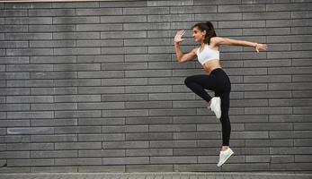 Photo in motion. Young sportive brunette with slim body shape against brick wall in the city at daytime