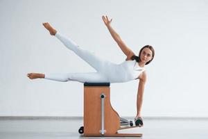 Leaning on the side. Confident young sporty woman with slim body type in the healthy center doing exercises by using special equipment photo