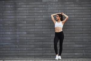 Young sportive brunette with slim body shape against brick wall in the city at daytime photo