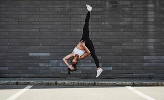 haciendo parkour loco y acrobacias atléticas. joven morena deportiva con forma de cuerpo delgado contra la pared de ladrillo en la ciudad durante el día foto